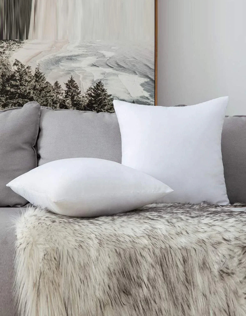 Weiße Kissen auf grauem Sofa mit Felldecke und Waldbild im Hintergrund